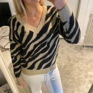 Zebra stickad tröja - Mysig stickad tröja i beige och svart med zebra mönster. Man kan ha den på bpda hållen. Den har någon liten defekt.
