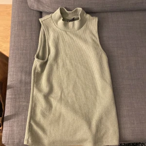 Grönt linne - Ett grönt linne med en kort polokrage. Inköpt på Vero Moda och endast använd ett par tillfällen. Skönt och mjukt material med ett svagt ”ribbat” mönster.  Inköpt för 100 säljes för 40