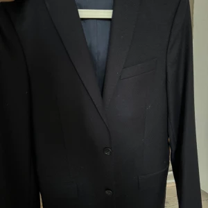 Jlindeberg, Navy Blazer, 46/Small  - Använd 1 gång, 9/10 skick. Otvättad så ser ut som ny, bara prislappen som saknas. Strl 46. Ev något kort i ärmarna, som kan vara bra att känna till om du har långa armar. Navy. Jlindeberg. Nypris: 3500kr. Köparen betalar frakt. 