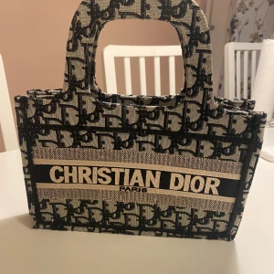 CD cool väska mindre design - Röd invändigt. Tyg och påsydd loga. Originalfärger. Tillhörande bred rem i tyg med monogram.  Hela väskan är i tyg inga print. 