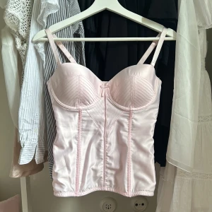 Korsett rosa - Rosa korsett i en perfekt rosa färg med gulddetaljer och en rosett i mitten. Älskar den men säljer då den är för liten. Köpt för 600kr. Den passar både S och M då man kan bestämma hur bred den ska vara i ryggen