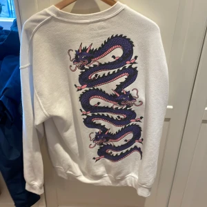 Vit sweatshirt med tryck på ryggen, storlek: M - Helt ok skick, använd kanske 3-4 gånger Den har en fläck på vänsterarmen