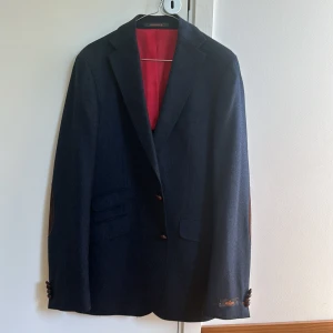 Ny Kavaj Morris str 148 - Mörkblå kavaj från Morris Helt ny och aldrig använd Har aldrig använts då den är för lång i ärmarna för mig (jag väger ca 77kg och är 179cm lång)  80% ull 20% polyamide Detaljer i läder Herrmodell Storlek: 148