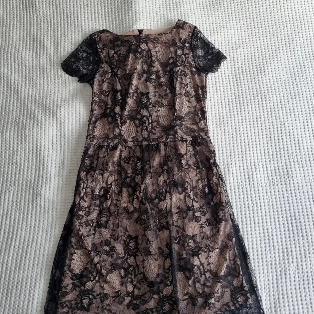 Omfamna tidlös elegans med denna mellanlånga klänning från Steilmann, där det klassiska möter det chic! Med en beige underkjol prydd med intrikat svart spetsöverdrag är denna klänning epitome av sofistikation.. Klänningar.