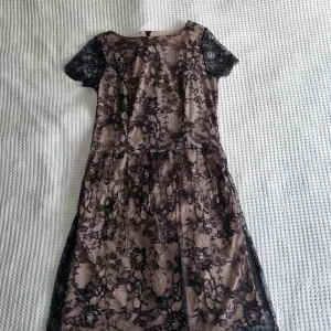 Steilmann klänning - Omfamna tidlös elegans med denna mellanlånga klänning från Steilmann, där det klassiska möter det chic! Med en beige underkjol prydd med intrikat svart spetsöverdrag är denna klänning epitome av sofistikation.