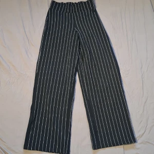 Polyester byxor - Svarta polyester byxor med vita ränder. Strech i midjan, raka och baggy i modellen. Storlek XS