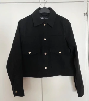 Svart kort jacka skjortjacka kappa blazer kavaj knappar fickor stockholmsstil stockholmstil - En svart jacka i storlek XS från Zara. Stängs med tryckknappar fram.  Fint skick och sparsamt använd. Lite luddig i tyget på vissa ställen, men syns endast när man kollar nära.