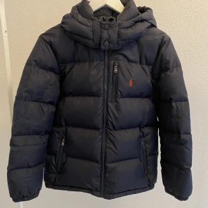 Marinblå Ralph Lauren jacka - Vinterjacka från Ralph Lauren i storlek L/G (14-16) 160/80. Marinblå med rött Ralph Lauren märke. Sparsamt använd i mycket bra skick. Nypris: 2995kr! 💙 Köparen står för frakten.