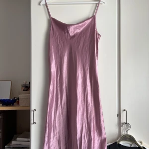 Satinklänning - Lilarosa satinklänninh med djup rygg. Köpt second hand, fint skick och använd en gång av mig. Draperad/hängande tyg i fram över bysten. Supersnygg och unik färg! Står ingen storlek, men den passar mig bra och brukar ha S. Kan nog också passa M