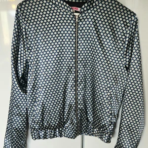 Cardigan Indiska stl M - Jättefint skick, med dragkedja och två fickor på magen. Mönstret var svårfotograferat, men sista bilden tycker jag blev mest rättvis. Fin glansig polyester. Fungerar lika bra som cardigan, som lätt sommarjacka. Den går i blått/ljusgrönt/vitt/svart.