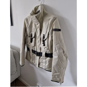 Woolrich  - Jättesnygg jacka från Woolrich. Size M. Helt otroligt välarbetad.  Slejfar, fickor, bälte, sömnad. Fantastiskt figursmickrande.  Finns en fläck nedtill framtill som inte är behandlad.  Knappen högst upp har släppt på ena sidan men är helt intakt