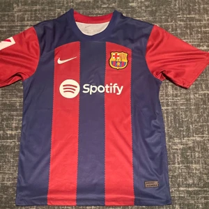 FC BARCELONA 23/24 HEMMA TRÖJA - Tjena, säljer min Barcelona tröja med Pedri 8. P:et i Pedri är tejpat och strykt med strykjärn så att det sitter fast pga av att det förra lossnade…