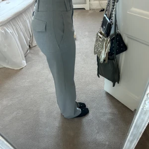 Grå kostymbyxa  - Säljer ett par ljusgrå kostymbyxor med fickor på rumpan!! Supersöta! Mid/lowwaist på mig som brukar ha 32-34 i byxor! Skriv för fler foton!!💕