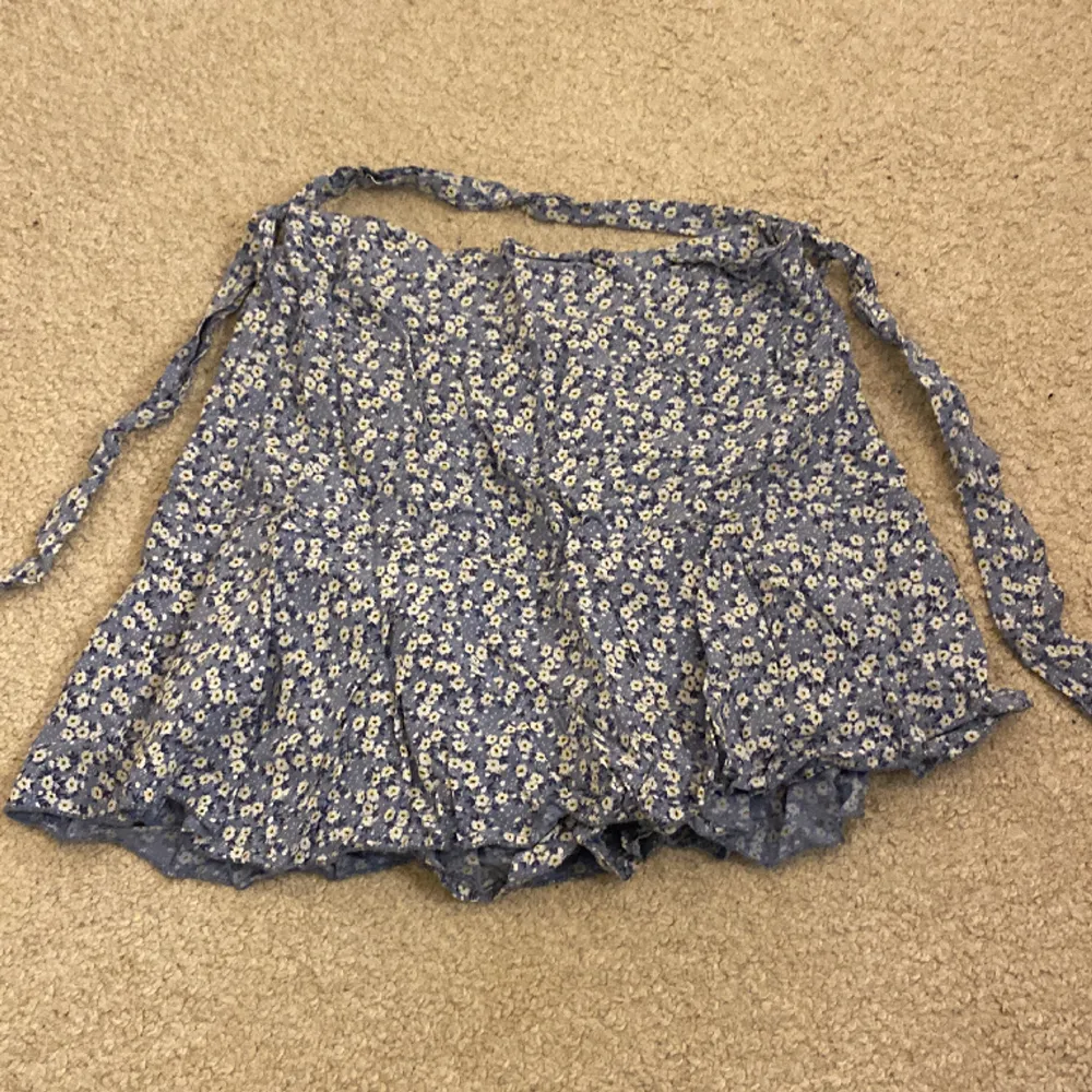 En blommig ljusblå kjol med inbyggda shorts. Kommer ursprungligen från en marknad utomlands. Använder ett fåtal,  gånger. Insydd i midjan också men går lätt att sprätta . Kjolar.