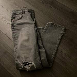 Grå jeans med hål vid knäna å liten slits där nere, strl 36