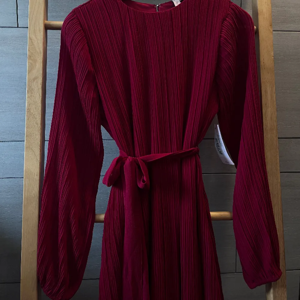 Härlig röd långärmad klänning med plisserat tyg, midjeband och puffiga ärmar. Plaggets längd är 86 cm (från axelsömmen till fållen) och klänningen slutar strax ovanför knäna. Aldrig använd och lapparna sitter kvar. Storlek 36 ❤️. Klänningar.