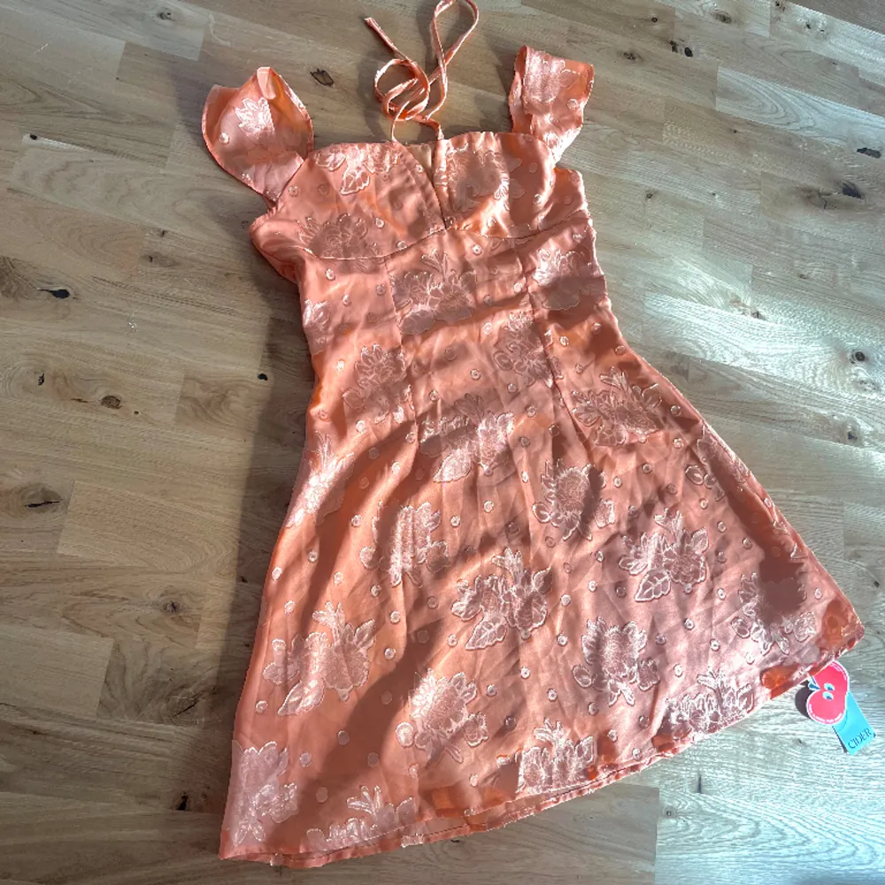 Vacker orange miniklänning med diskret blommigt mönster på🧡 Aldrig använd, därav att lappen sitter kvar. Köpt från Cider, storlek S✨. Klänningar.