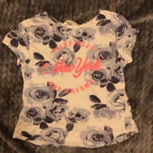 T-shirt - En blå tröja med lite mörkare blå blommor och neon råda text 