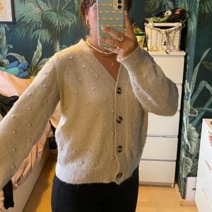 Vit stickad cardigan  - En benvit kofta som man knäpper i fram. Så söt detalj med små ”bollar” som är stickade i tröjan. Så skön i materialet och värmande. Inte så djup i urringningen. 