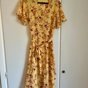 Somrig klänning  - Gul klänning med röda blommor. Somrig och härlig med fint fall. Fint skick. Köpt på Kappahl. 