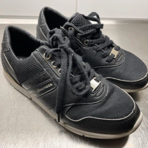Tommy Hilfiger sneakers - Tommy Hilfiger svarta sneakers med guldfärgade detaljer, använda ett fåtal gånger, säljes. 