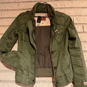 Khujo vårjacka  - Snygg militärgrön vårjacka från Khujo i mycket bra skick.  Strl: S Färg: Grön  