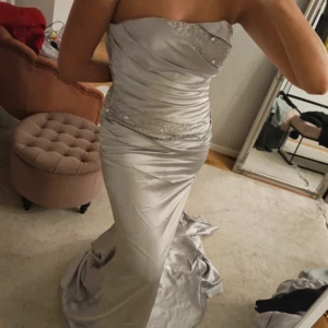 Silvrig Balklänning - Jättefin balklänning i storlek M, använd en gång och är i jättebra skick. Jag är 172 och den går till golvet på mig (utan klackar). Man kan bestämma lite själv hur tajt den ska sitta eftersom det är en korsett upptill💗