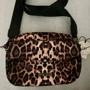 *NY*Axelremsväska ”Bag Leopard One Size” Fr Don Donna - Ny oanvänd med prislapp.  Mindre axelremsväska med tre fack, två mindre och ett större i mitten. Bredare axelrem som går att knäppa loss. Emblem i silver. Kraftigt smuts/vätskeavvisande material.  Nypris: 499 kr, Pris nu: 230 kr