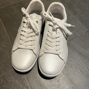 Lacoste sneakers  - Vita Lacoste sneakers med guldiga detaljer. Använda 2 gånger, nästan nyskick, lite smutsig närmre sulan. Säljer då de är för små för mig.