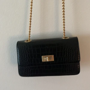 Svart väska med guldkedja - Köpt för två år sen, använd ca 3 ggr. Kedjan-110cm Bredd-19cm Höjd-13cm