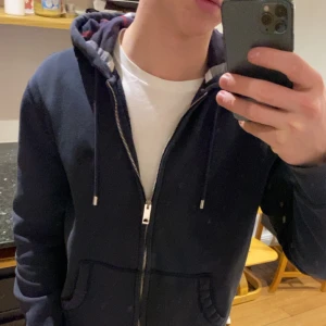 Burberry Hoodie navy  - Tja! Säljer nu denna snygga burberry zip Hoodie i storlek m, den passar dock även s lika bra 😊, köpt från heatnlux. På andra bilden ser du bättre hur färgen är på den 😊. Bra skick förutom att den är lite nopprig på insidan, annars fint skick! 