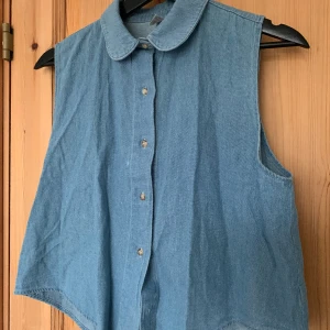 Ärmlös blus i jeanstyg - Ärmlös jeansskjorta i fint skick. Minimala fläckar på framsidan, syns knappt. Axelbredd 34cm Längd 58cm Bredd nedtill 51cm