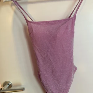Glittrig baddräkt/body - Glittrig rosa baddräkt med öppen rygg, kan utan tvekan användas som en body med ett par snygga byxor till! Oanvänd 