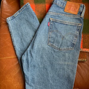 Levis 501 jeans - Levis 501 i klassisk mellanblå tvätt. Tidlös färg! W28 L28 Mellanhög midja 99% bomull, 1% elastan vilket gör byxorna följsamma men ändå rejäla.  Mått enligt nedan:  Midja mätt rakt över: 37cm Innerbenslängd: 70cm