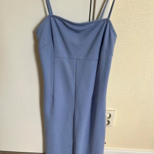 Ljusblå klänning med smala axelband - En elegant ljusblå klänning med smala axelband. Klänningen har en enkel och stilren design med en rak passform och ärmlös stil.