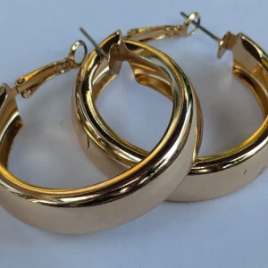 Guldfärgade hoop-örhängen - Ett par guldfärgade hoop-örhängen med en slät och blank yta. Örhängena har en klassisk rund form och är av medelstorlek.i fint skick, färgen blekare eller rostig (se sista bilden).