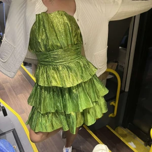 Cool grönskimmrig festklänning - Jätte snygg glittrig/skimmrig grön volangklänning! Köpt vintage och ger mycket studio 54 vibez! Statement klänning! Endast använd en gång! Tyget har lossnat lite vid mitten men det syns inte och går lätt att så ihop med bara några stygn!