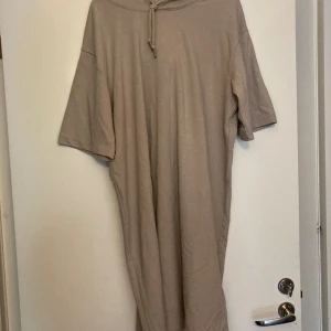 Beige mjukisklänning  - Beige mjukisklänning med korta ärmar och luva med dragsko. Helt ny. Från H&M