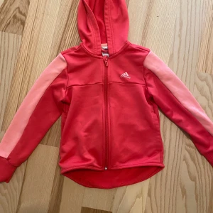 Huvtröja/jacka Adidas - Strl 7-8 år. Rosa/korall. Begagnat skick.  Tyvärr är det ett streck från en färgpenna på ena ärmens baksida (se bild). Inget som man tänker på eller direkt märks när den sitter på.  Kolla gärna in mina andra annonser för samfrakt.