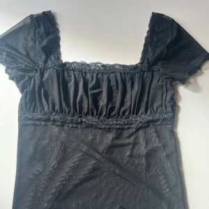 Svart topp i mesh - Söt svart topp med spetsdetaljer. Toppen har korta ärmar och en rund halsringning. Storlek s från Topshop, har endast använts ett par gånger.