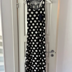 Prickig lång klänning - Prickig klänning svart, vit med en blå ficka på bröstet. Stl. L 