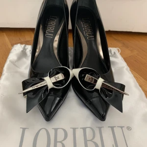 Svarta lack klackskor med med vit och silver detalj - Svarta lack klackskor med vit och silverdetalj på tån. Blåa sulor. Mycket fint skick. Jag kan träffas i centrala Stockholm eller skicka. Storlek 36. 