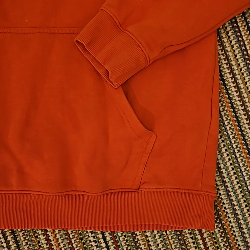 En orange hoodie med en logga på ena bröstet. Ingen design på ryggen.. Hoodies.