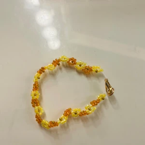 armband - detta är ett hemmagjort pärlarmband med blommor! orange och gul🧡💛  gör dessa armband av stort intresse och i bra skick!