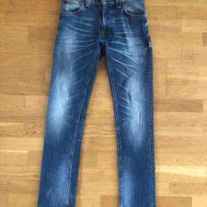 Nudie Jeans - Ett par riktigt snygga Nudies i mörkblå med en skön wash och utan slitningar. Säljes på grund av att de var för små för mig i midjan, kom dm för mer beskrivningar på mått och liknande. Pris kan sänkas vid snabb affär!