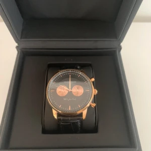 Grand Frank Stockholm klocka - Mycket fint skick.  En djärv svart urtavla, ett rosenfodral och ett mönstrat läder tar dig till nästa nivå. Denna klocka är givetvis vattentät upp till 5ATM, har reptåligt glas och en kropp i rostfritt stål.  Nya pris 2 229kr