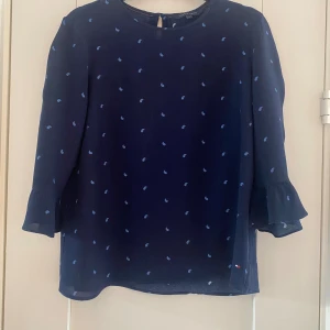 Marinblå blus i viskos med 3/4 trumpetärmar från Tommy Hilfiger i strl 4(34). - Marinblå blus i viskos med 3/4 trumpetärmar från Tommy Hilfiger i strl 4(34).  Använd men i fint begagnat skick.  Mått Över bröstet: ca 48 cm Längd från axeln och ner: ca 58 cm  100% viskos  Kommer från ett djur och rökfritt hem.