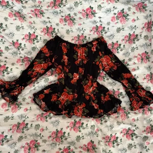Blommig off-shoulder blus - En svart off-shoulder blus med röda blommor med lätt utsvängda armar samt volang vid ärnslut och nedtill från H&M i strl XS!💓