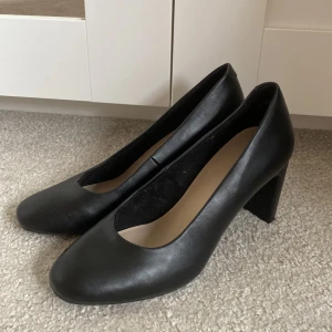 svarta skor med klack - Svarta klackar med skinn imitation. Klacken är cirka 5 cm. Har använts en gång.