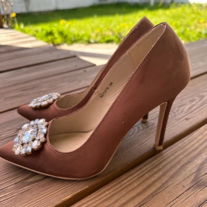 Stiliga pumps från NELLY - Snygga och stiliga pumps från Nelly i storlek 38, har broscher på som sitter utmärkt på plats .. använd några gånger.  